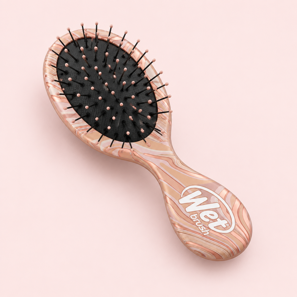 Angled view of Wet Brush Mini Detangler Engineered Nature Pink on a blush background