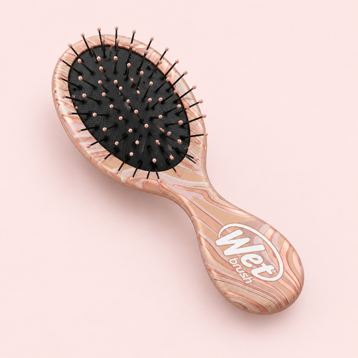 Angled view of Wet Brush Mini Detangler Engineered Nature Pink on a blush background